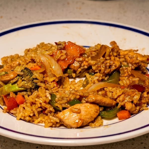 Chicken fried rice with broccoli, carrots, and onions on a white plate with a blue rim.