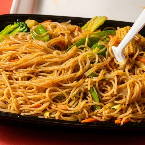 Chow mein noodles with broccoli, carrots, and snow peas in a black takeout container with a fork.