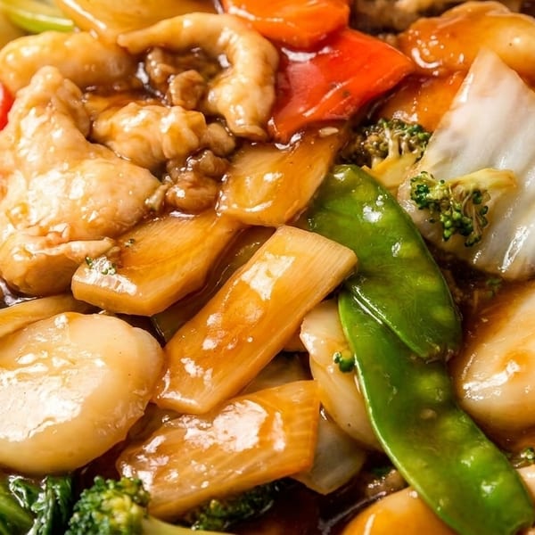 Close-up of chicken and mixed vegetables in a savory brown sauce, including broccoli, snow peas, and bok choy.